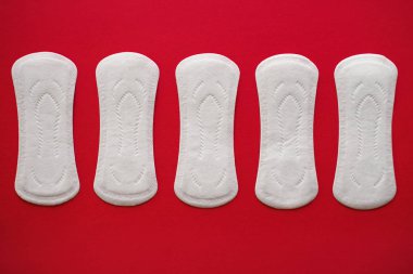 Five menstrual pads for women on a red background, top view