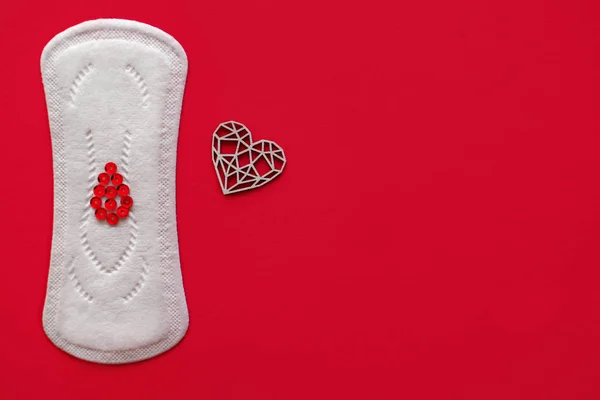 Menstrual pad with red sequins in the shape of a heart on a red background, top view, miniature of the menstrual period — Stock Fotó