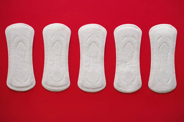 Cinco almohadillas menstruales para mujeres sobre un fondo rojo, vista superior —  Fotos de Stock