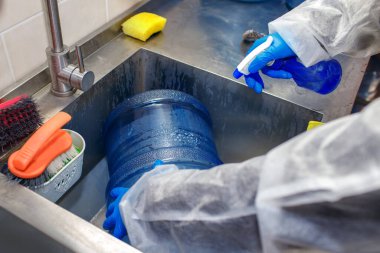Fabrika işçisi su basıncının altında büyük bir plastik şişeyi yıkıyor, bir işçi özel kıyafetler giyiyor, plastik temizliyor, mükemmel temizlik için özel ürünler, içme suyu üretimi