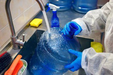 Bir fabrika işçisi su basıncının altında büyük bir plastik şişeyi yıkar, bir işçi özel kıyafetler giyer, plastiği temizler, mükemmel temizlik için özel ürünler, plastik geri dönüşümü sağlar.