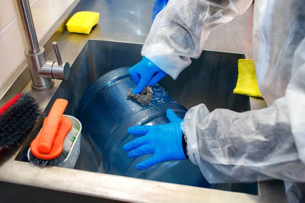 Fabrika işçisi su basıncının altında büyük bir plastik şişeyi yıkıyor, bir işçi özel kıyafetler giyiyor, plastik temizliyor, mükemmel temizlik için özel ürünler, içme suyu üretimi