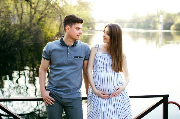 Hamile bir kız ve erkek arkadaşı rıhtımda oturuyorlar ve birbirlerine bakıyorlar, güzel bir nehir ve gün batımı, müstakbel ebeveynler dışarıda vakit geçiriyorlar, güzel genç bir anne, mutlu bir baba.