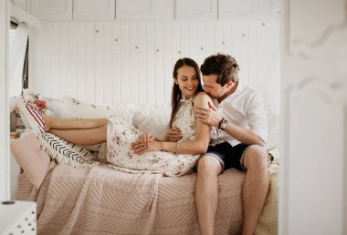 Beyaz bir odada poz veren güzel genç bir çift, bir erkek kız arkadaşına sarıldı, kız ona yaslandı, genç insanlar gülüp eğlenirken, bir erkek bir kadını öptü.