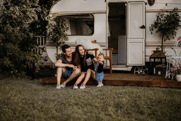 a young family meets the sunset near their mobile home, dad, mom and daughter, a young girl holds her daughter in her arms, her husband sits nearby and hugs his wife, the family travels