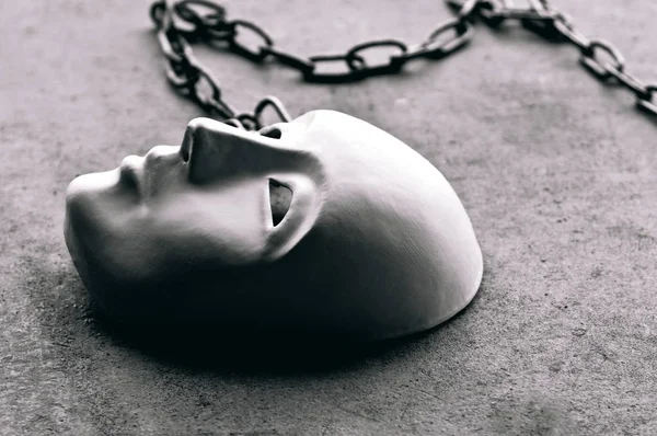 Alçı taşı maskesi yere zincirlenmiş, sanatsal görüntü, maskenin altında yaşayan ya da maskesini düşürmüş insanların düşüncesi, umursamazlık duyguları, maskenin altındaki hayat, maskenin üzerindeki zincir.