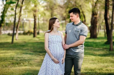 Genç hamile anne ve erkek arkadaşı parkta yürüyorlar, karı koca çocuk beklentisiyle dışarı çıkıyorlar, güzel bir bahar havası, şık bir çift, bir erkek bir kadını öpüyor.