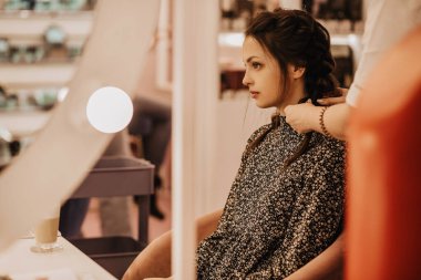 Kadınlar salonundaki genç bir kadın bir kuaförün hizmetinden yararlanıyor, saçını örüyor, şık bir saç stili, profesyonel bir kuaför esmer, kahverengi bir renkle çalışıyor.