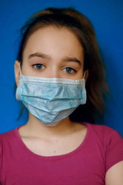 A girl in a protective medical mask from a virus on a blue background, pandemic, coronovirus infection, Covid-19, the global epidemic, protection against coronovirus, airborne infection
