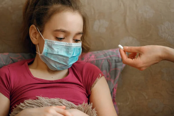 A girl in a protective mask became infected with a coronovirus, quarantine, a doctor gives a pill, a sad child, Covid-19 virus, airborne droplets, a worldwide pandemic, flu, treatment for the disease