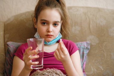 Virüs yüzünden koruyucu maskeli hasta bir kız Coronovirus tedavisi, hava enfeksiyonu tedavisi için hazırlanıyor. Covid 19, kız karantinada, elinde bir bardak su tutuyor.