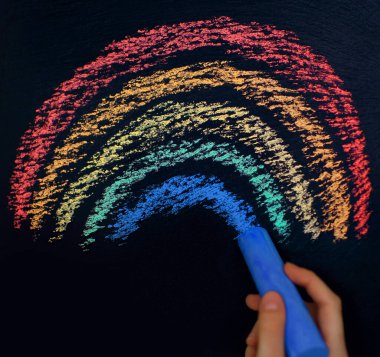 Siyah bir arkaplanda renkli tebeşirle gökkuşağı çizimi, bir çocuk gökkuşağı çizer, yaratıcı gelişim için bir resim, yazı tahtası arkaplanı, yazı için bir yer, eğitim