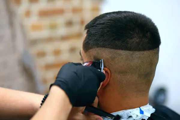 professional hairdresser doing hairstyle to man with electric razor in mens salon, fashion guy, stylish man, back view