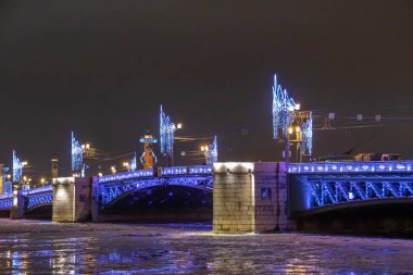 Neva Nehri 'nin kıyısındaki dekore edilmiş saray köprüsünün görüntüsü. Köprünün karşısındaki St. Petersburg 'daki Rostral sütunlarına bakın. Kentteki köprüde Noel aydınlatması.