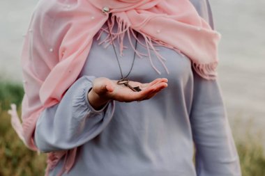 Eşarplı kız elinde anahtar olan bir kolye tutuyor.