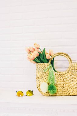 Beyaz tuğlalı arka planda çiçek ve güneş gözlüğü olan büyük bir bambu çantası.