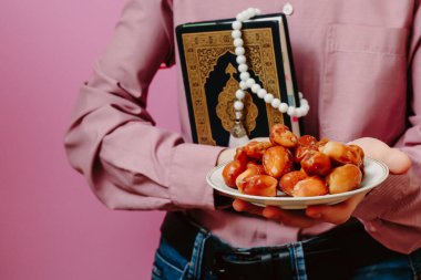 Adamın elinde kutsal Kur 'an, İslam tespihi ve tarihler var. Pembe bir arka planda.
