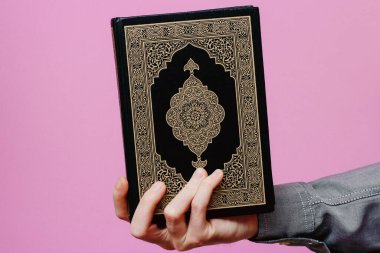 Adamın elinde kutsal Kur 'an var. Pembe bir arka planda.