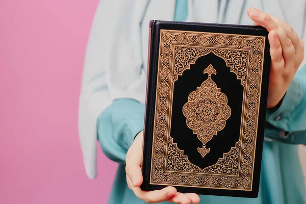 头戴头巾的穆斯林妇女手里拿着一本粉色背景的古兰经 — 图库照片