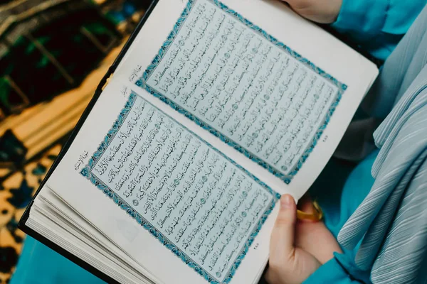 Türbanlı Müslüman bir kadın pembe bir arka planda Kuran tutuyor.