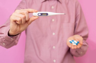 Adamın elinde termometre, diğerinde de el hapları var. Hastalık. Isı.