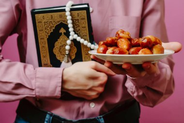 Adamın elinde kutsal Kur 'an, İslam tespihi ve tarihler var. Pembe bir arka planda.
