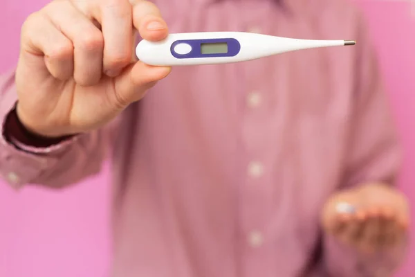 The guy holds a thermometer, and in the other hand pills. Disease. Heat.