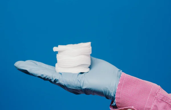 A guy in a medical glove holds cotton pads. Blue background. Medical and cosmetology content