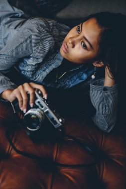 Güzel kız onun elinde fotoğraf makinesi ile deri koltukta yalan