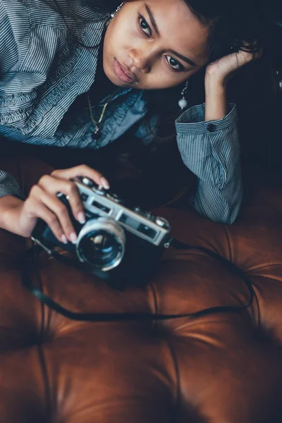 Superbe fille couchée sur un canapé en cuir avec un appareil photo dans ses mains — Photo