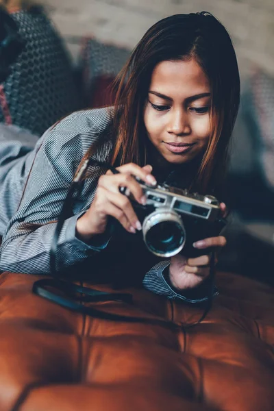 Splendida ragazza sdraiata sul divano in pelle con fotocamera fotografica nelle sue mani — Foto Stock