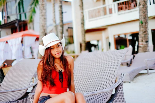Mulher bonita sentada na cama de sol com o chapéu no resort de praia, férias de verão — Fotografia de Stock