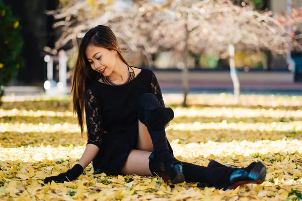 Menina bonita em vestido vintage preto e luva de mão. Mulher de vestido retro brincando no parque com folhas de ginko. Lábios vermelhos — Fotografia de Stock