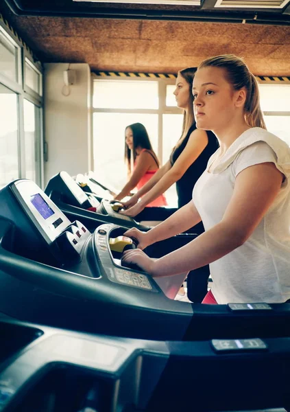 Fitness girl burning calories on the treadmill. Beautiful young cheerful girl in sportswear exercising on treadmill at gym with other girls