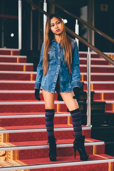 Mulher na moda jovem em calça azul, e meias de joelho listradas longas que descem em escadas com o carpete vermelho — Fotografia de Stock
