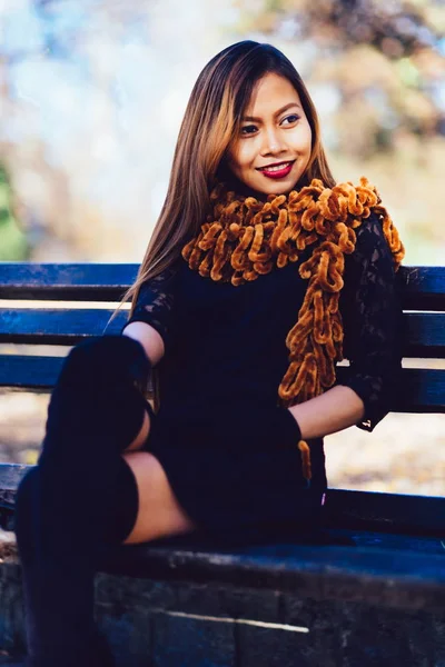 Menina bonita nova em vestido preto com cachecol marrom sentado no banco — Fotografia de Stock