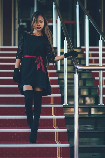 Jovem mulher elegante em vestido preto andando em escadas com o tapete vermelho — Fotografia de Stock