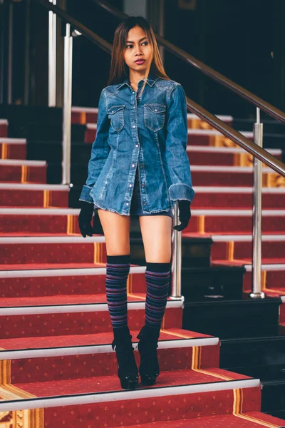 Mulher na moda jovem em calça azul, e meias de joelho listradas longas que descem em escadas com o carpete vermelho — Fotografia de Stock