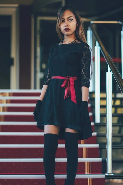 Jovem mulher elegante em vestido preto andando em escadas com o tapete vermelho — Fotografia de Stock