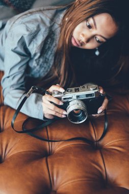 Eski Vintage retro film kamera onun elinde tutan deri kanepe yatan muhteşem bir genç kadın. Şık kadın Retro tarzı