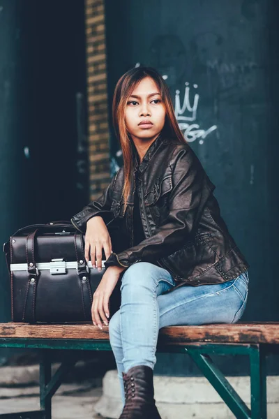 Gorgeous young woman in leather jacket, sitting on the bench posing with leather bag, hipster, Vintage Retro style — Stock Photo, Image