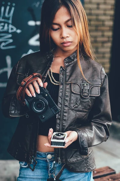 Splendida giovane donna in giacca di pelle, tenendo fotocamera fotografica e contatore della luce. Hipster, stile vintage retrò — Foto Stock