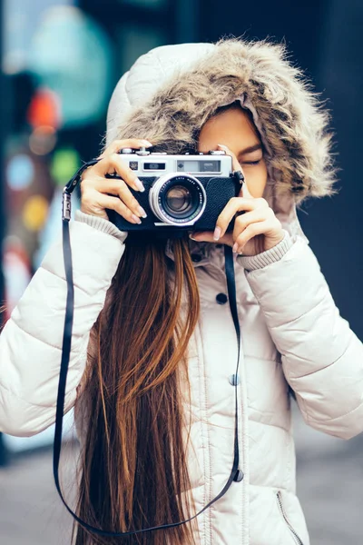Beautiful girl in a winter coat photographing outside using Vintage Retro film camera. urban environment — Stock Photo, Image
