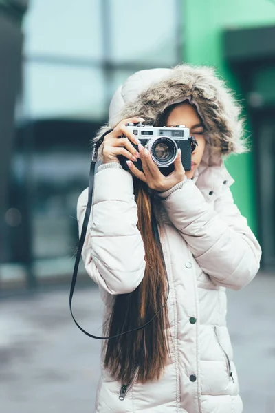 Beautiful girl in a winter coat photographing outside using Vintage Retro film camera. urban environment — Stock Photo, Image