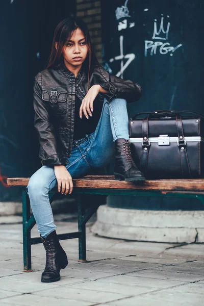 Linda jovem mulher em jaqueta de couro, sentado no banco posando com saco de couro, hipster, estilo Vintage Retro — Fotografia de Stock