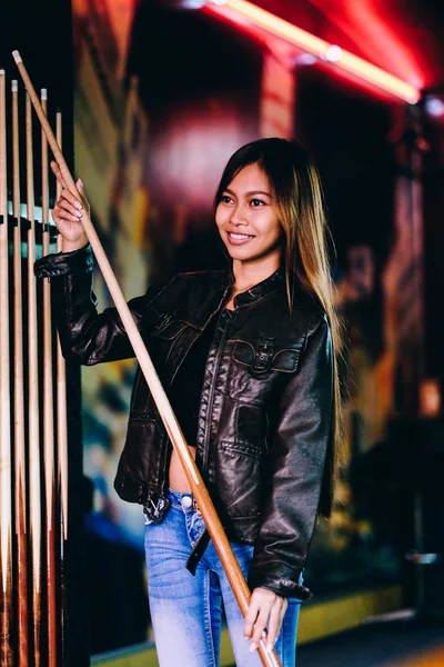 Menina bonita nova vestindo jaqueta de couro em um clube de bilhar, com cue stick se preparando para o jogo — Fotografia de Stock