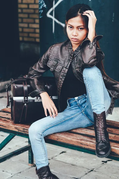 Menina lindo em jaqueta de couro sentado no banco com o saco de couro, estilo hipster — Fotografia de Stock