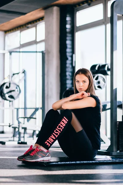 Vonzó karcsú női csinál, nyújtó gyakorlatok, fekete Matt, a modern fitneszközpontban. Fáradt lány pihentető az intenzív edzés után — Stock Fotó