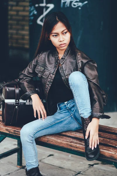 Menina lindo em jaqueta de couro sentado no banco com o saco de couro, estilo hipster — Fotografia de Stock