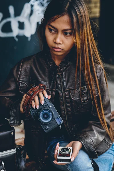 Cool girl in leather jacket holding photo camera and light meter in her hand. Girl hipster style — Stock Photo, Image